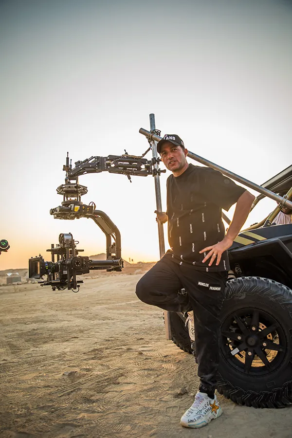 Waleed Nassif beside a camera car crane rig on a desert set at sunset