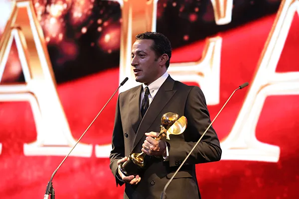 Waleed Nassif holding an award trophy at the microphone