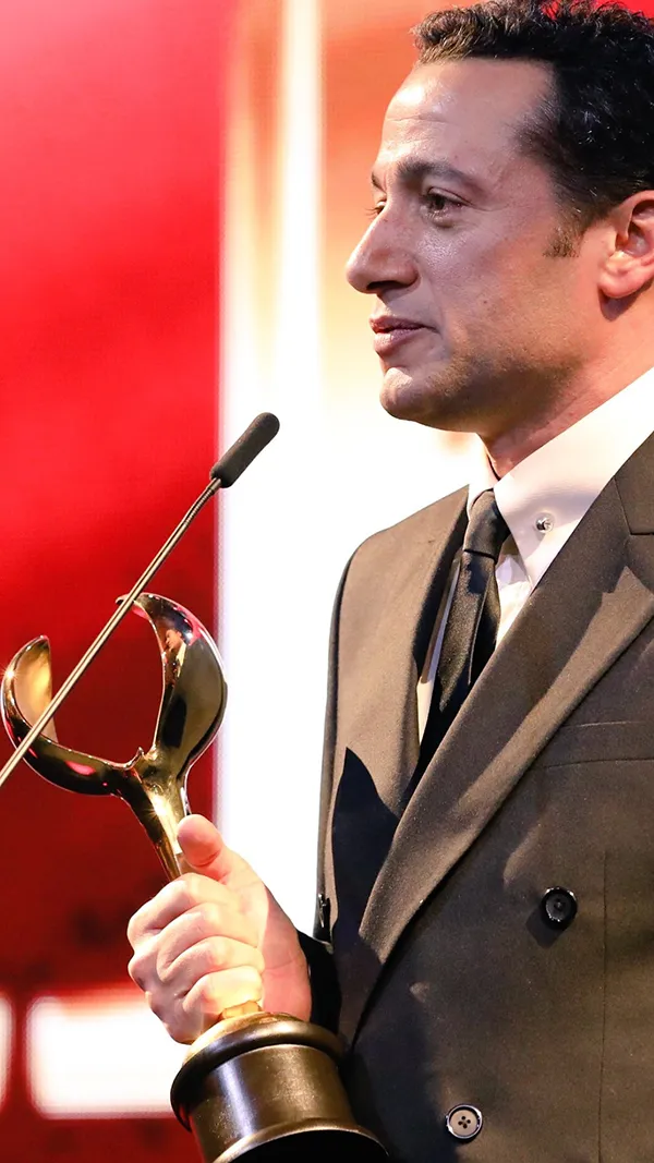 Waleed Nassif in profile with an award trophy at the microphone