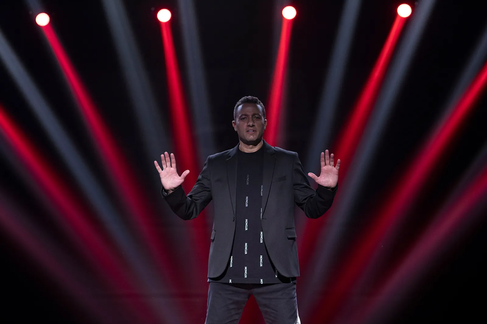 Waleed Nassif on stage with palms raised under red and white light beams