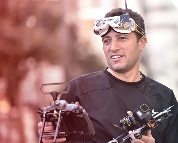 Waleed Nassif holding a racing drone and controller, FPV goggles on his forehead