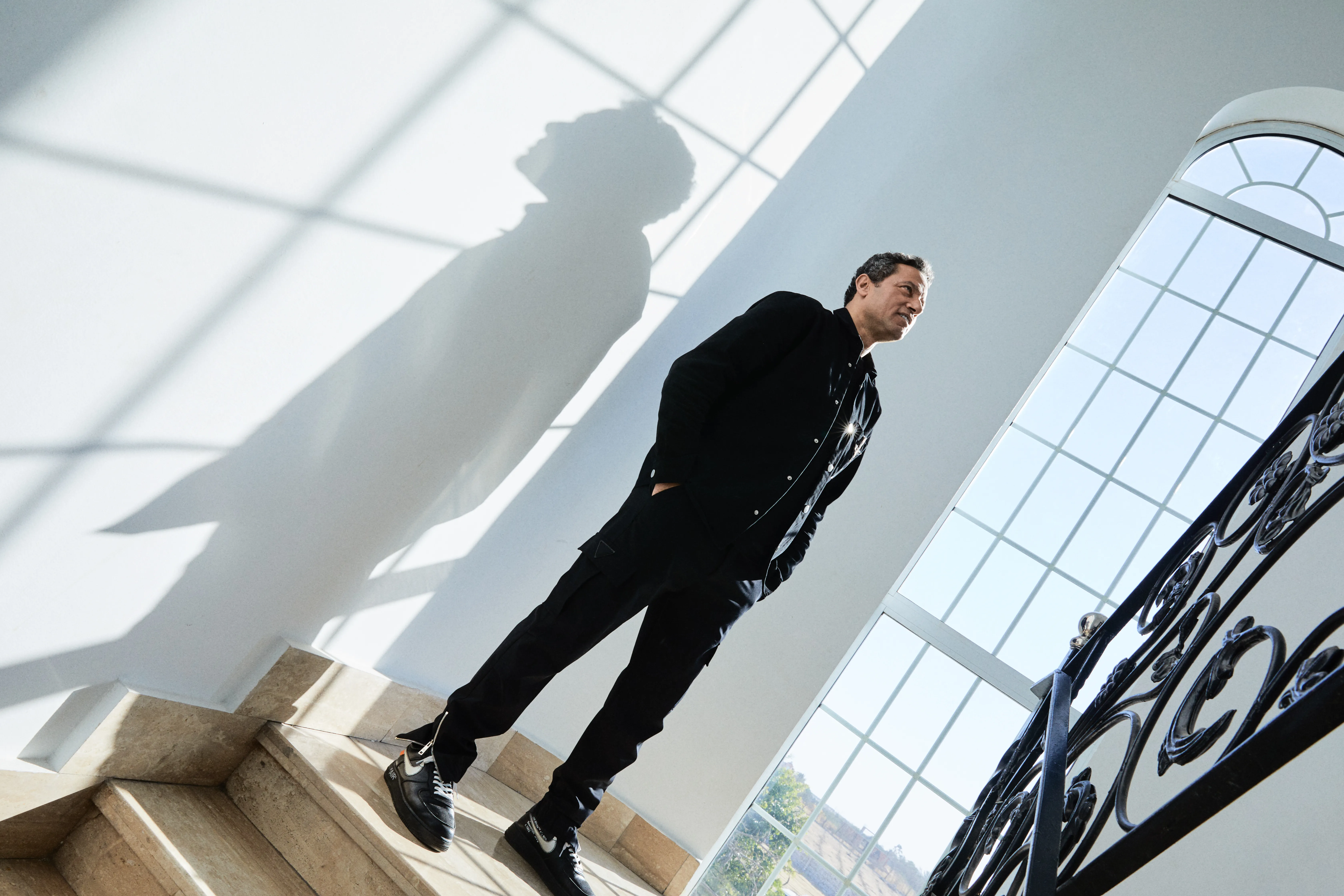 Waleed Nassif standing on a sunlit staircase beside tall arched windows