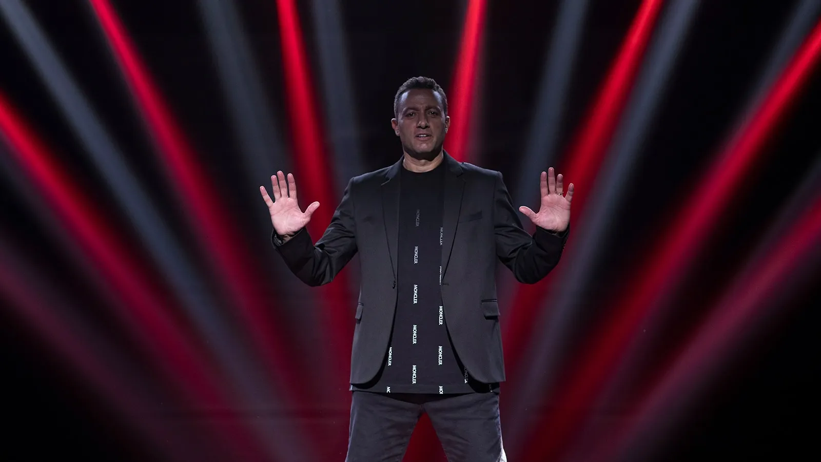 Waleed Nassif on stage with palms raised under red and white light beams