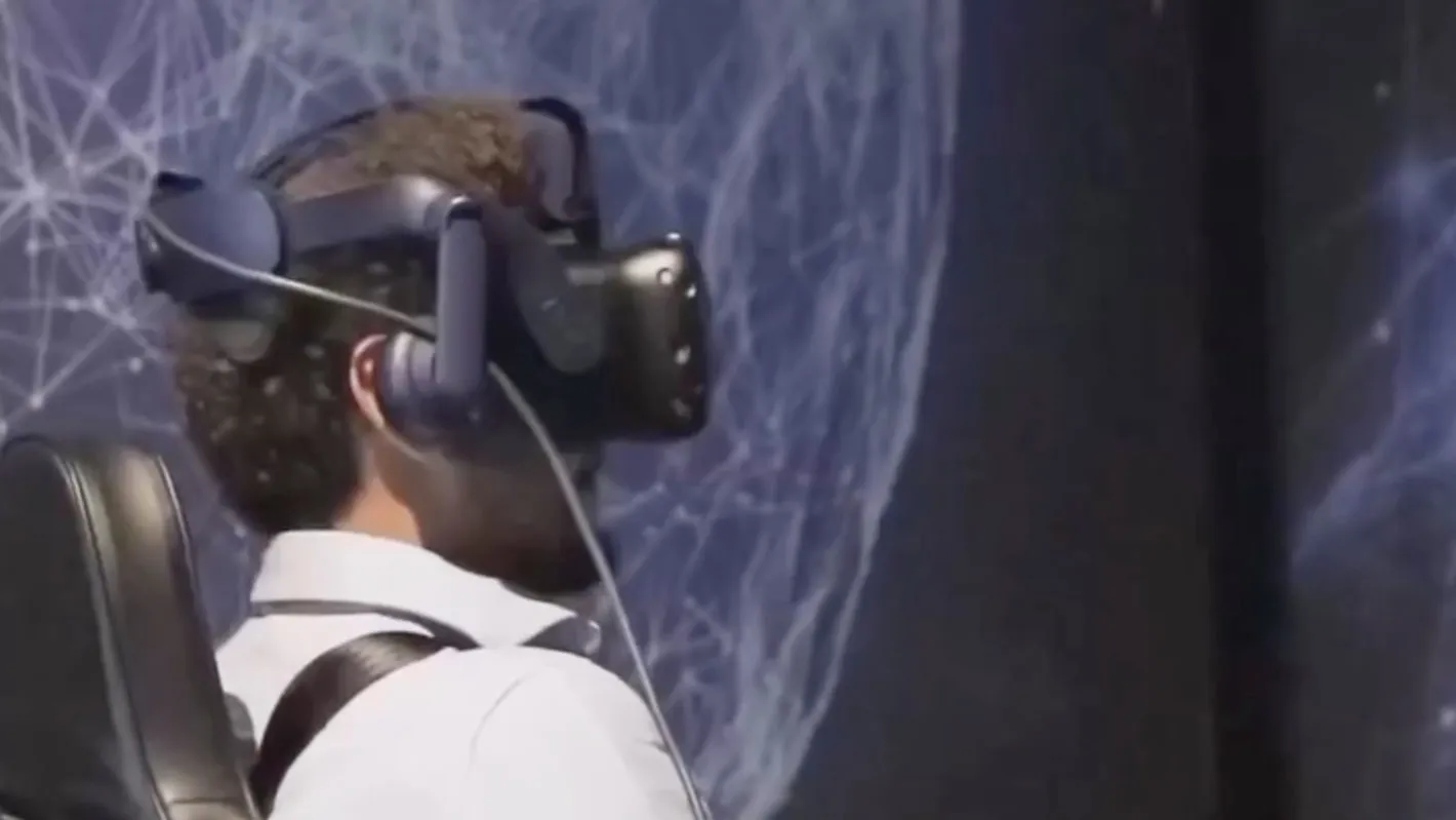A seated visitor wearing a VR headset in front of a projected network sphere, at a UAE 2071 VR experience