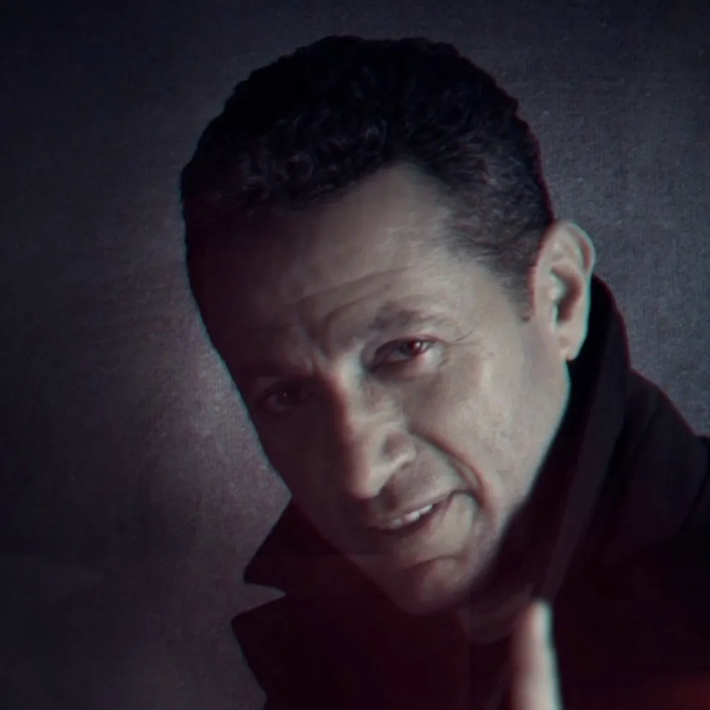 Waleed Nassif in a dark coat looking into the camera, in a blue-graded frame