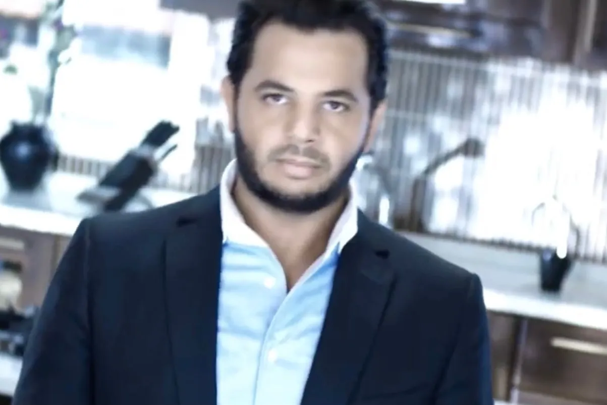 A bearded man in a dark suit and a light-blue shirt in a kitchen, from a public service announcement on drugs