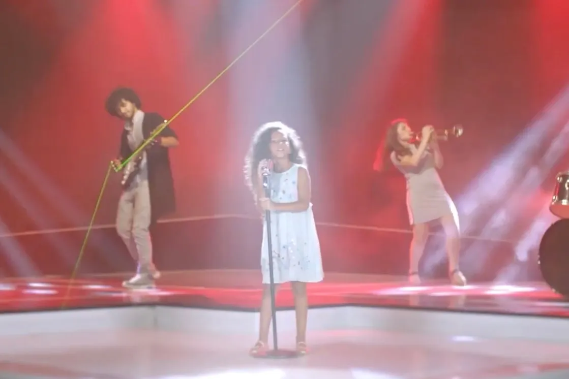 A young girl singing at a microphone on a red-lit stage, a guitarist and a trumpet player behind her, from the Matera Chocolate ad